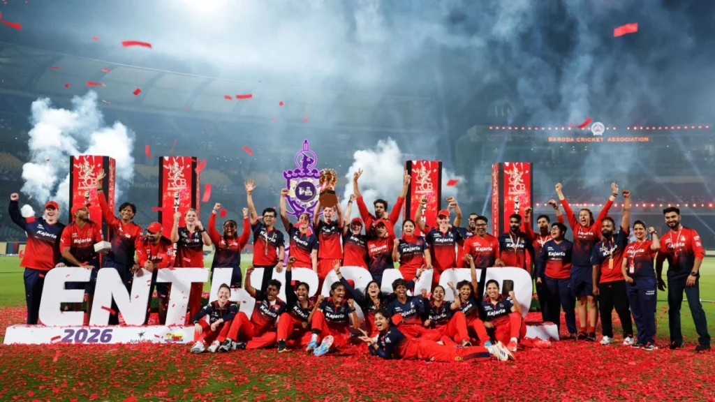 Smriti Mandhana and Sophie Devine celebrating with the WPL 2026 trophy after RCB’s final victory
